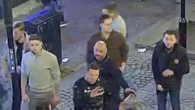 A blurry CCTV image taken from above of seven men in a high street.