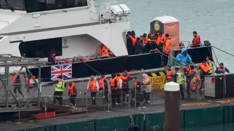 Gareth Fuller/PA Media A group of people in life jackets being brought off a boat into a docking area