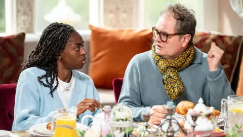 Cat Burns and Alan Carr sitting at the breakfast table on The Celebrity Traitors