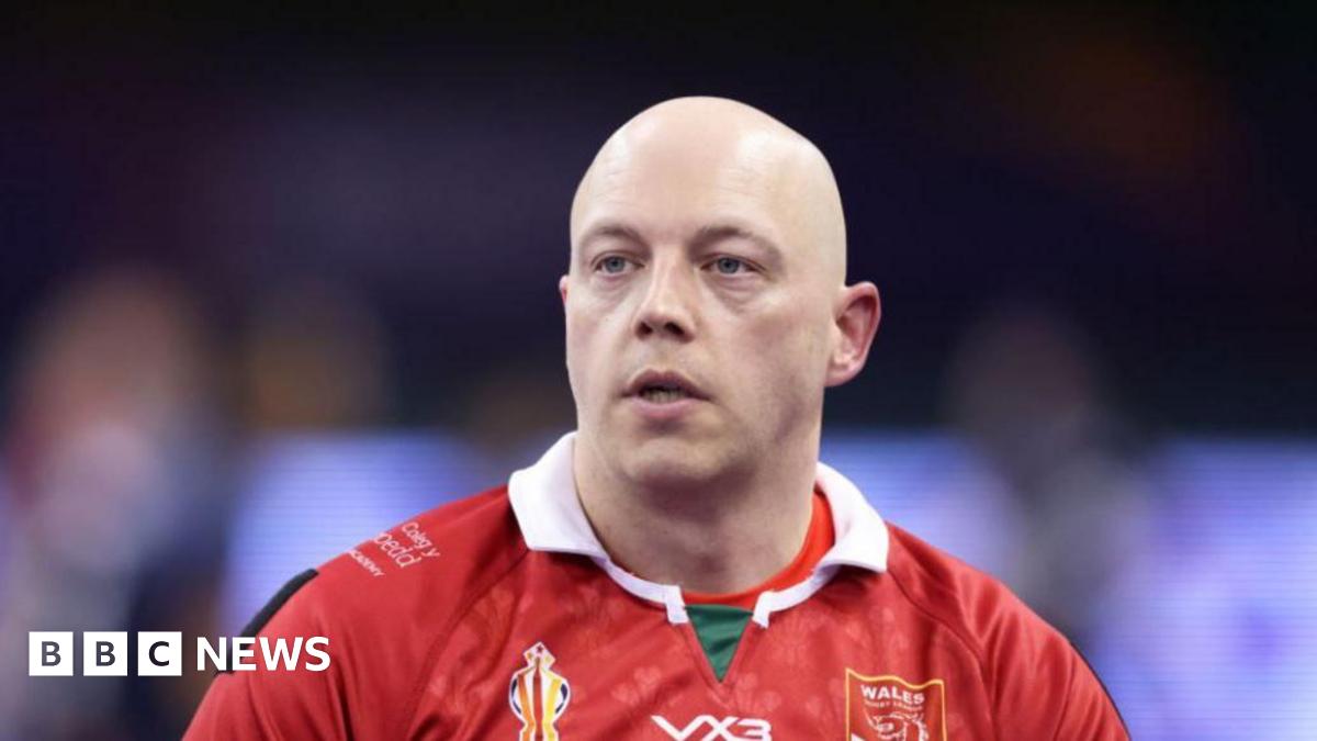 A brown NC500 sign post which says it is 27 miles to Ullapool next to a country road with hills in the background.