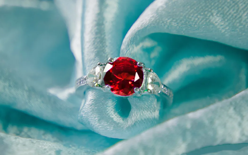 A red ruby gemstone ring on aqua-coloured fabric.