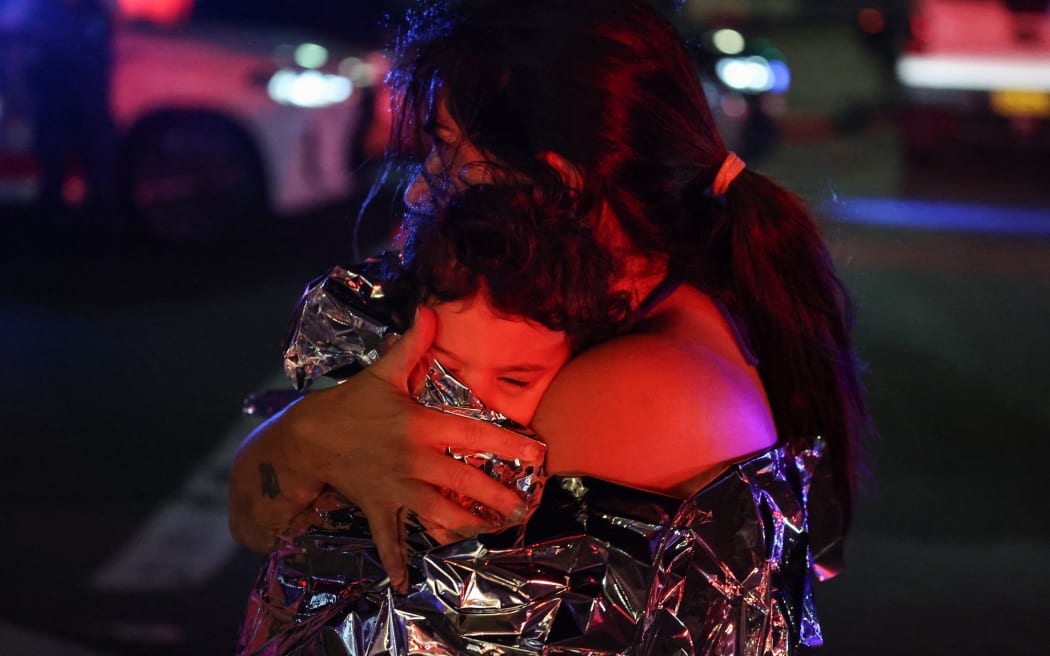 A woman holds her baby in a blanket after a shooting incident at Bondi Beach in Sydney on December 14, 2025. Australian police said two people were in custody following reports of multiple gunshots on December 14 at Sydney's famed Bondi Beach, urging the public to take shelter. (Photo by DAVID GRAY / AFP)