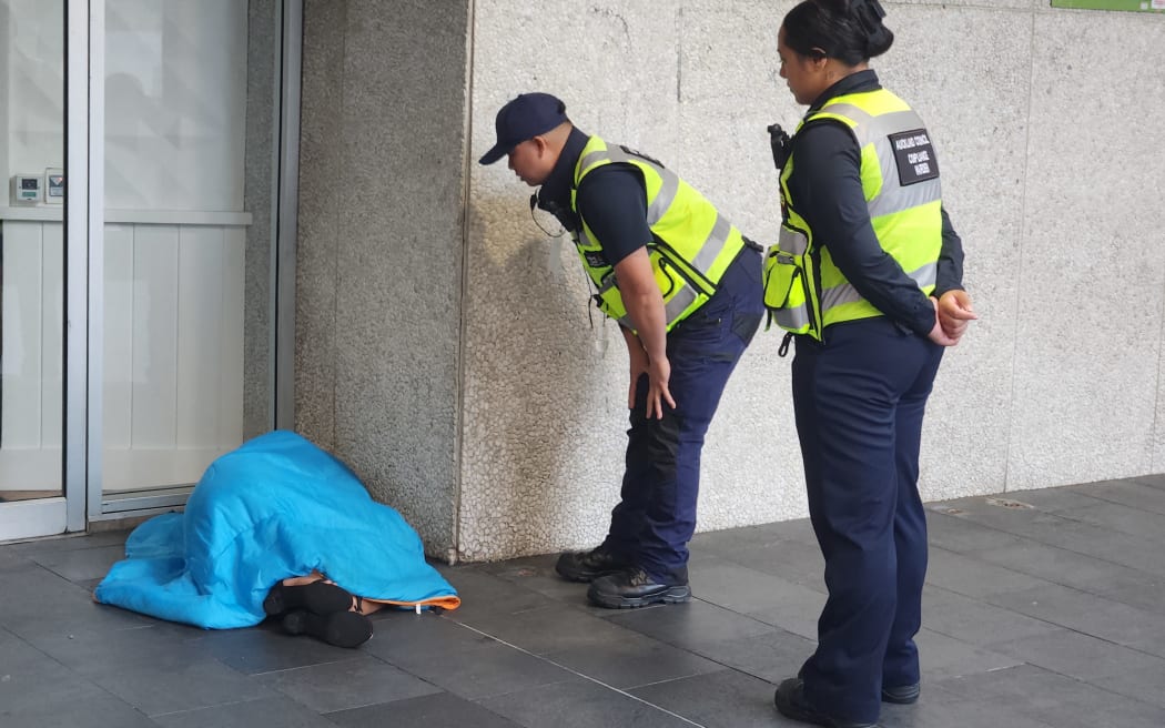 Auckland Council patrollers try to wake up a rough sleeper.