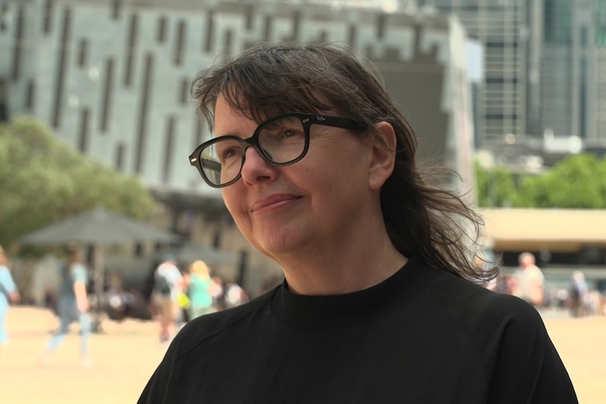 Katrina Sedgwick smiles while being interviewed at fed square, she is wearing black framed glasses and a black top