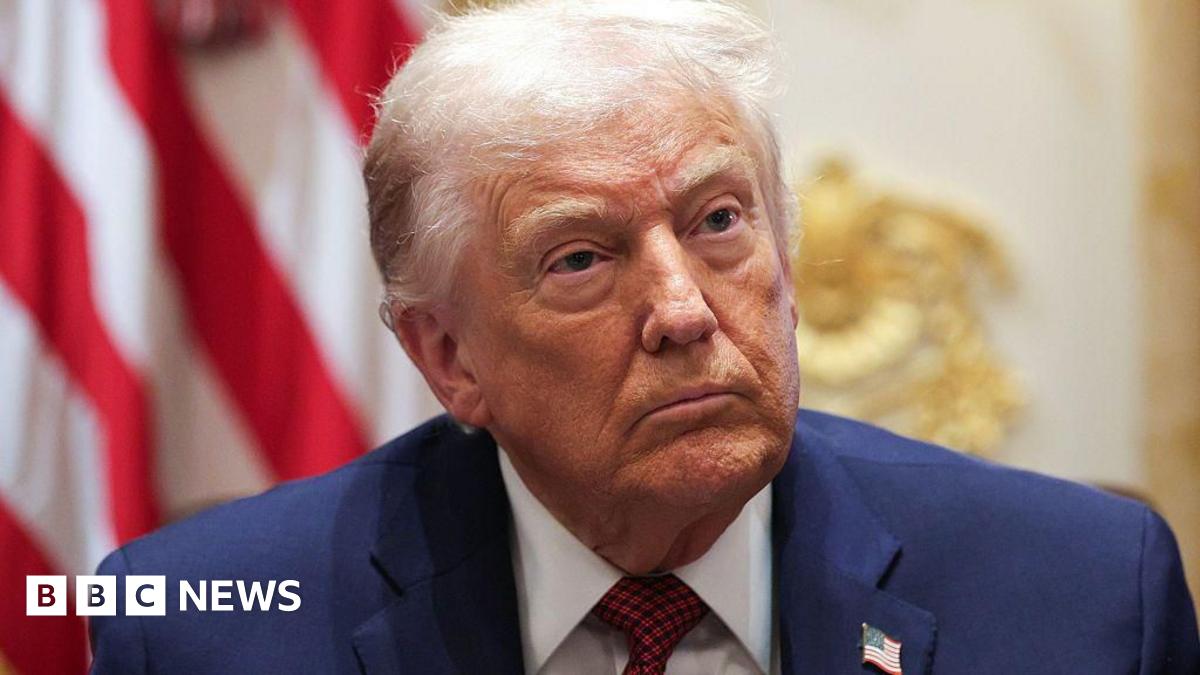 A brown NC500 sign post which says it is 27 miles to Ullapool next to a country road with hills in the background.