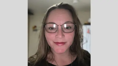 Heather Prindiville facing the camera in a screenshot taken from a Zoom conversation. She is wearing a dark top and dark red lipstick, and has shoulder-length brown hair