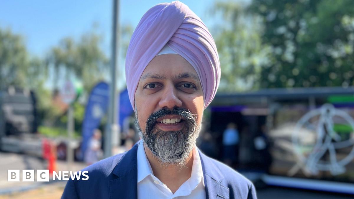 Slough MP Tan Dhesi is wearing a pink turban as well as a white shirt and navy suit. He is smiling and the pop-up heart clinic is visible in the background.