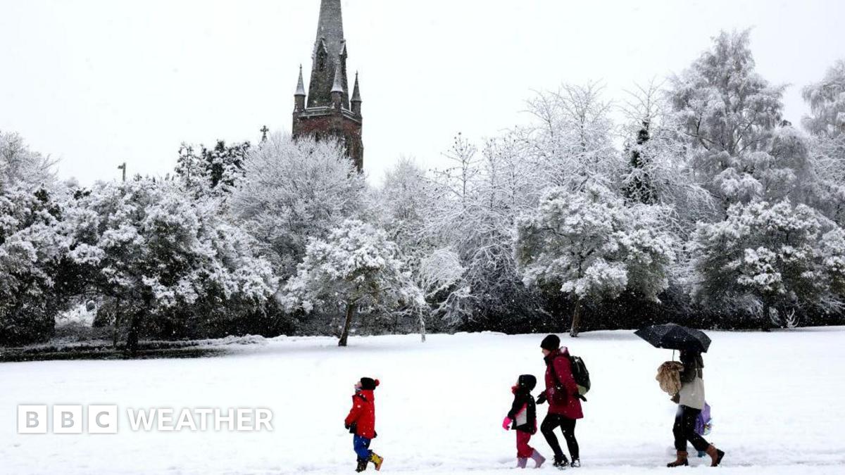 Snowy scene with a park area and a church in the background.  Trees covered in snow and a group of people walking in the snow.