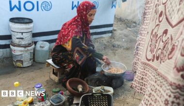 Displaced Palestinian woman Hanan Abu Taibah cooks food on a fire outside her  tent in Khan Younis, southern Gaza (18 December 2025)
