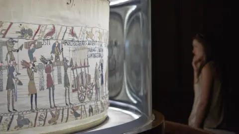 Getty Images The Bayeux Tapestry in Normandy is displayed in an upright glass channel that bends into an oval screen to allow all 58 scenes to be seen.