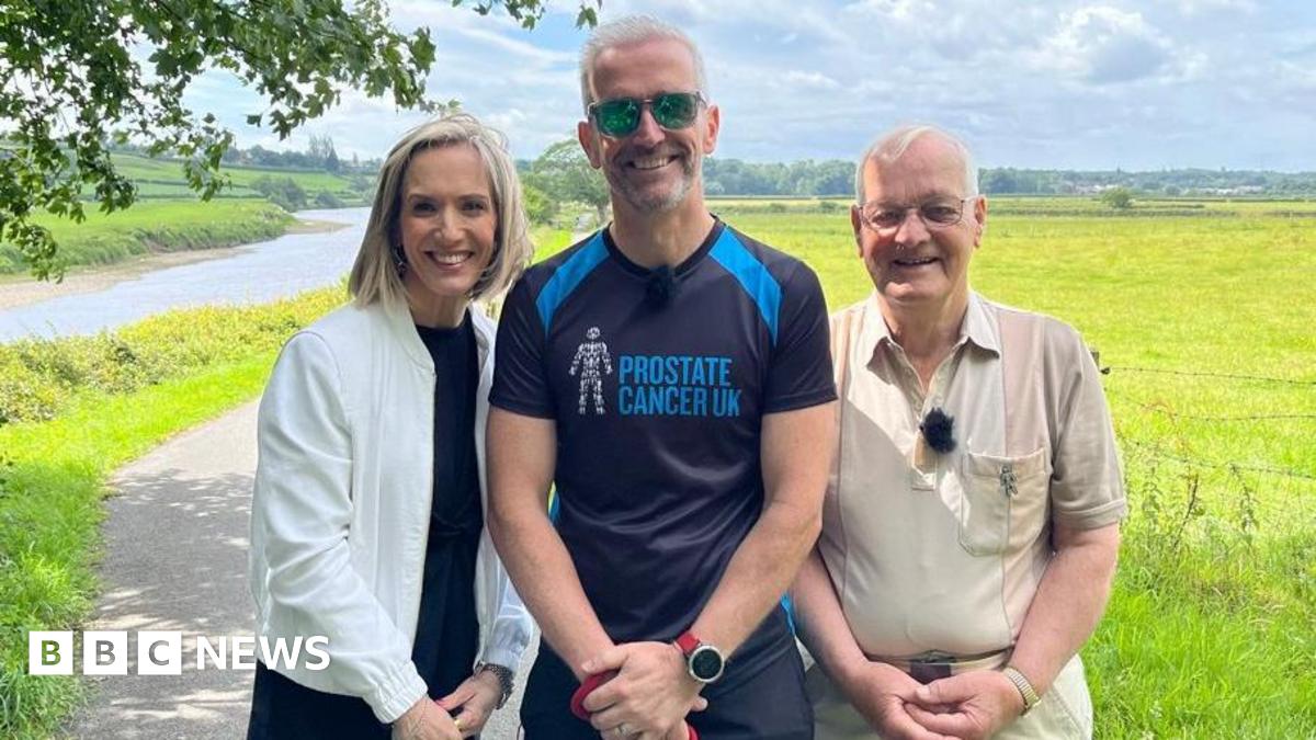 Michael Lilley is standing next to his father John and BBC North West Tonight's weather presenter Kay Crewdson on a path running through a field. He is wearing a T-shirt which says "Prostate Cancer UK".