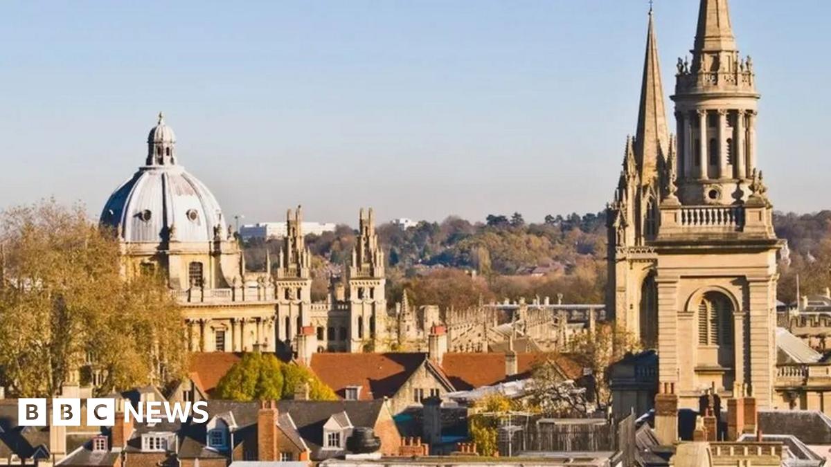 The skyline of the city of Oxford, in the UK. A large dome on the left is the Radcliffe Camera and a large steeple on the right is a university church. The sky is clear blue, and a variety of medeival buildings and colleges are dotted between the two landmarks.
