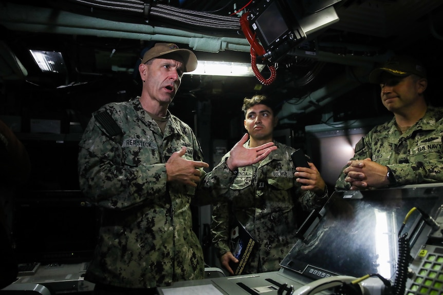 Men in US navy camo attire speak in a submarine.