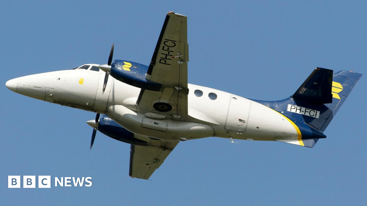 A white propeller aircraft with blue engines and a blue tail in front of a blue skyline