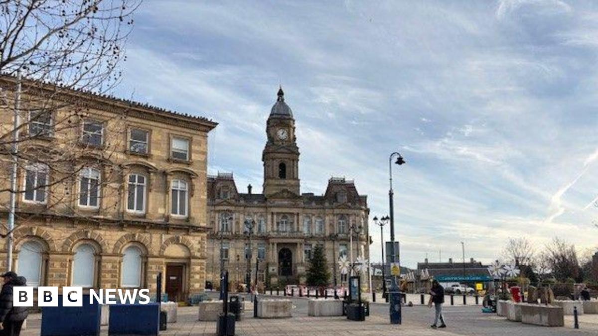 An artist's impression of a new park in Dewsbury, there is a large paved area with flower beds at each side and a grassed area, with people milling about and some fountains on the left.