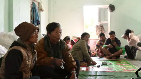 Civilians sit on the floor of a community centre in India