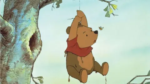 ZUMA Press, Inc./Alamy Illustration of Winnie the Pooh hanging by a rope from a tree with a perturbed look on his face