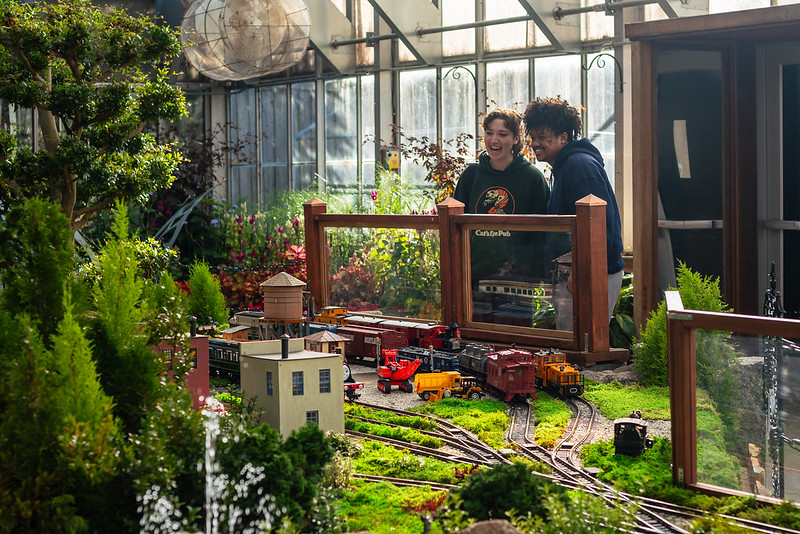 Two adults look at model trains in the Brookside Gardens conservatory