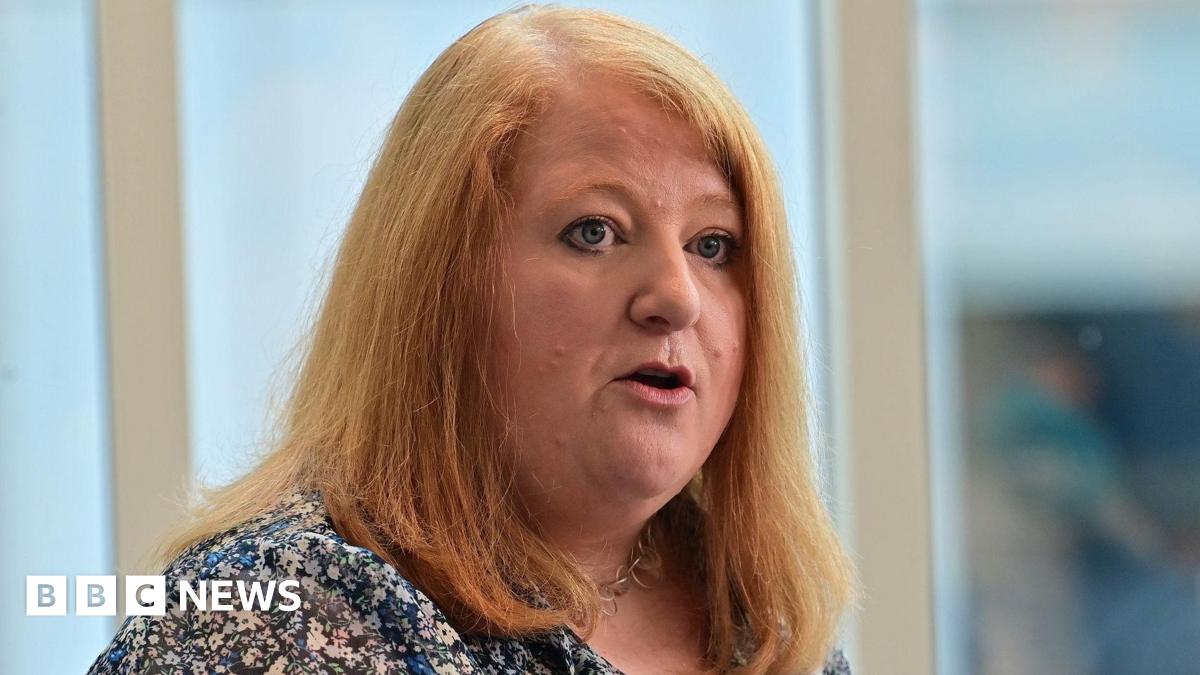 Naomi Long has long red hair and is wearing a flowery blouse