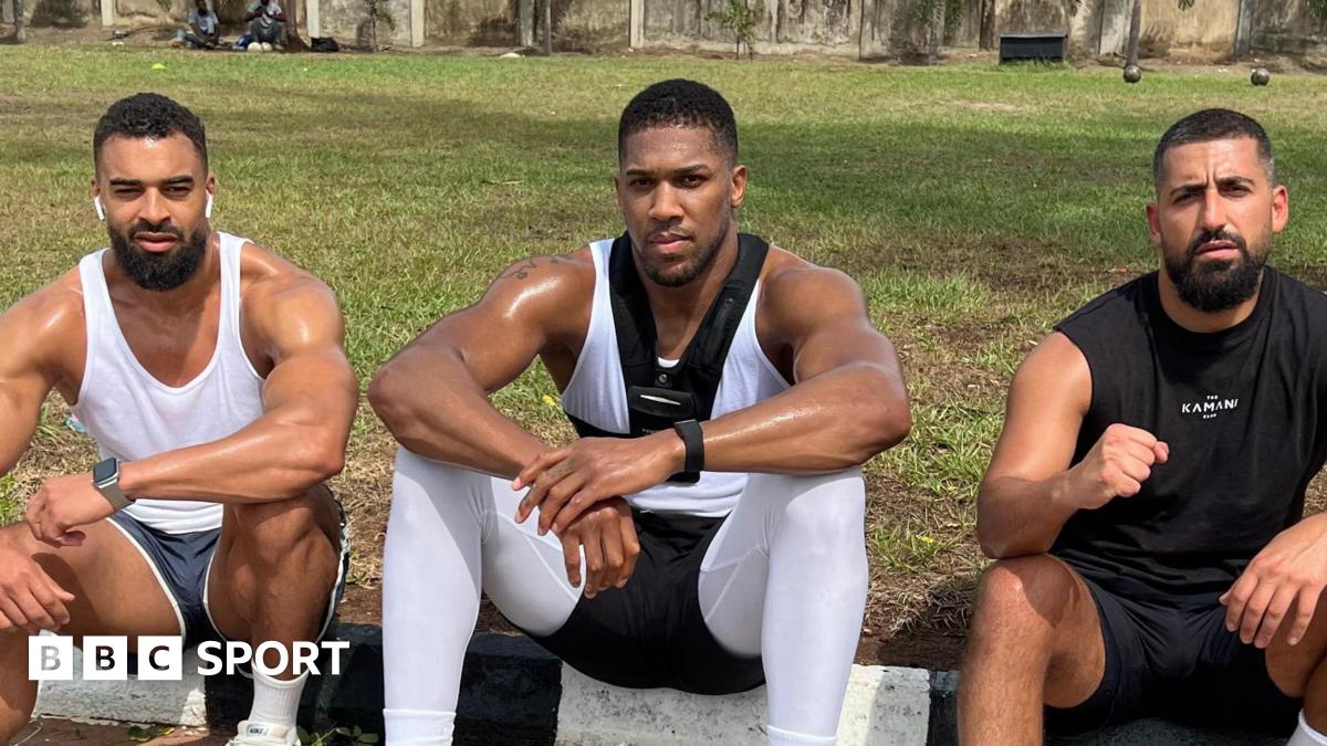 Anthony Joshua sits between Sina Ghami and Latif Ayodele as all wear training kit, with a grassy area behind the three men
