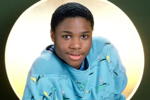 Getty Images Malcolm-Jamal Warner wearing a light blue sweatshirt with abstract and figure patterns.