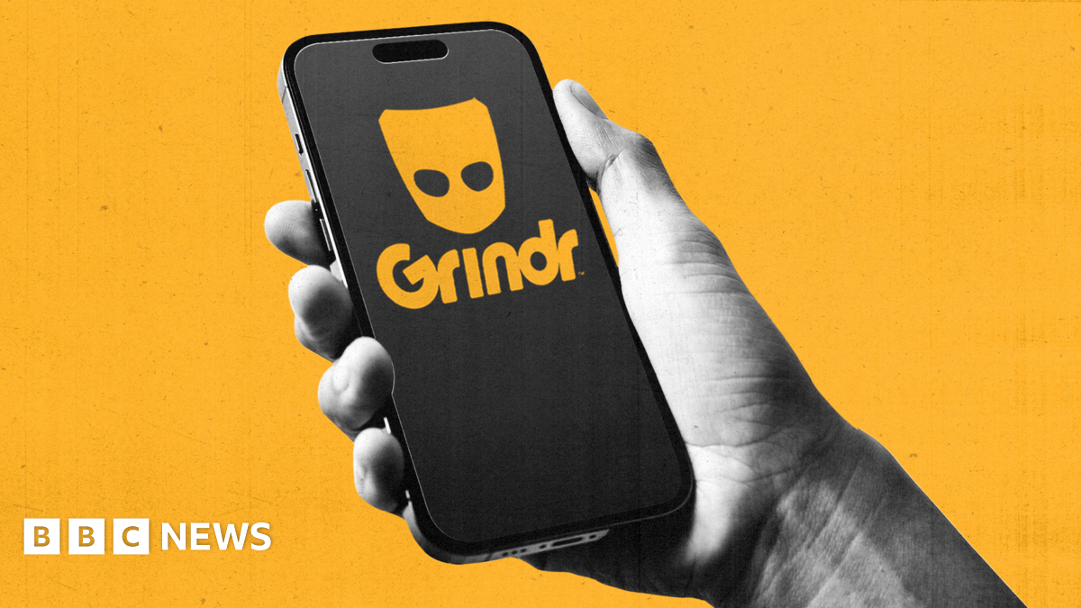 A hand holds a mobile phone with Grindr logo on it. Background is bright yellow.