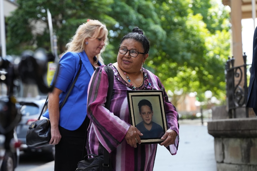 Woman smiles outside court hold a photo of a boy
