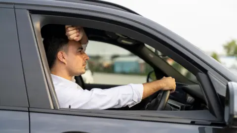 Getty Images A man looking frustrated while driving his car