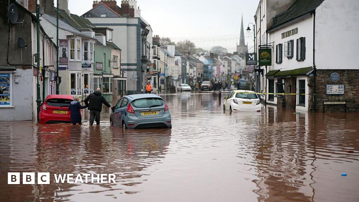 flooded street with cars submerged and a few people walking in the floodwater