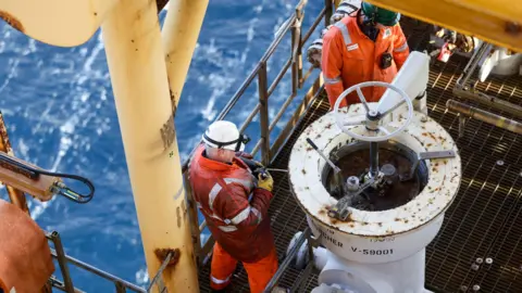 Getty Images Two workers wearing orange overalls and a hard hats fix a pig launcher on the Armada gas condensate platform, operated by BG Group Plc, in the North Sea, off the coast of Aberdeen.