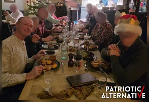 Patriotic Alternative Mr Lawler, with short hair and a vertically striped shirt, looks towards the camera at a Christmas dinner. He is sitting with eight other people, whose faces have been blurred 