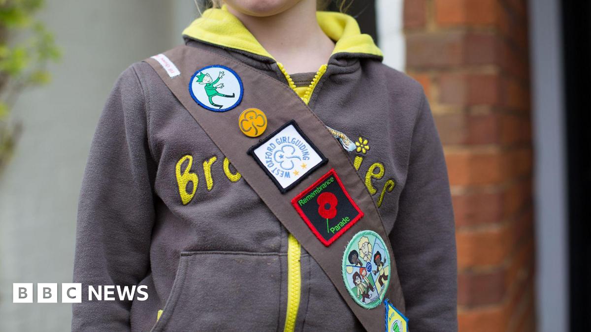 A girl wearing a brownies hoody and a sash with badges on