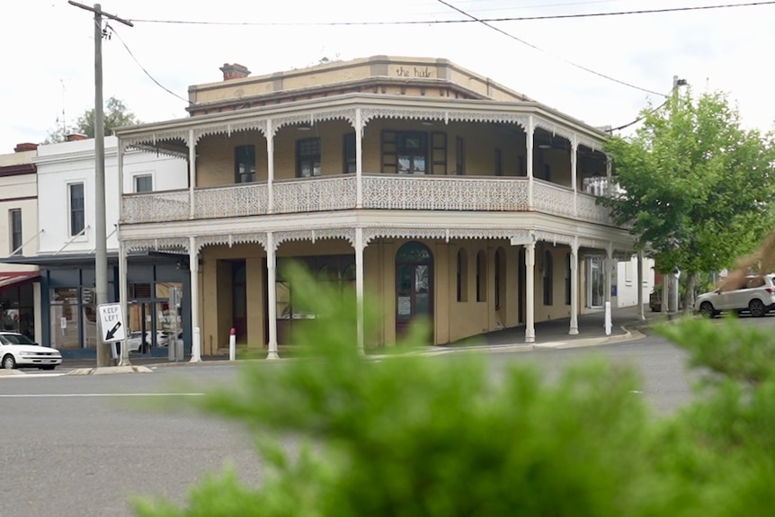 A view across a wide street of an attractive, two storey goldrush-era corner building with lattice ironwork.