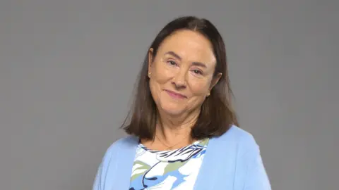 BBC Studios Scotland / Graeme Hunter A publicity shot of Arabella Weir as Beth from Two Doors Down. She gives a soft smile, her head slightly tilted and is wearing a pale blue cardigan and floral top.