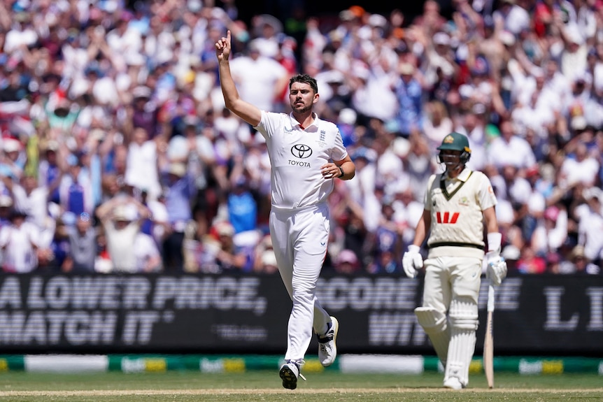 A cricketer in white holds his finger up in celebration with a batter next to him