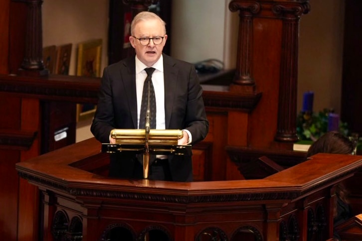 anthony albanese wearing a black suit and tie stands in a pulpit giving a eulogy.
