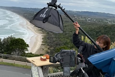 A man adjusts a light at a beach lookout for a photoshoot for a pastry.