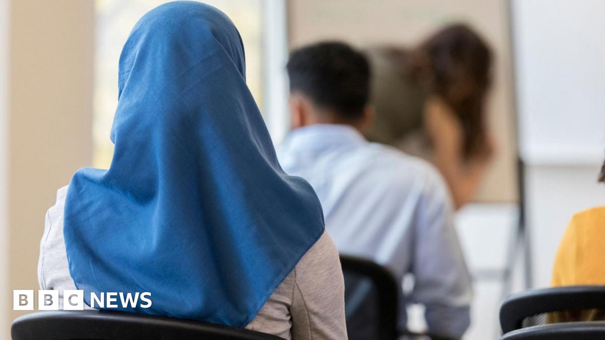 A woman wearing a blue headscarf seen from behind as she sits in a chair in a classroom