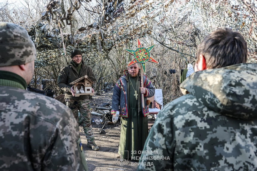 A Ukrainian army chaplain sings to uniformed soldiers holding a brightly coloured star.