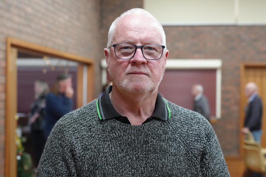A middle aged man with white hair and glasses in a hall. 