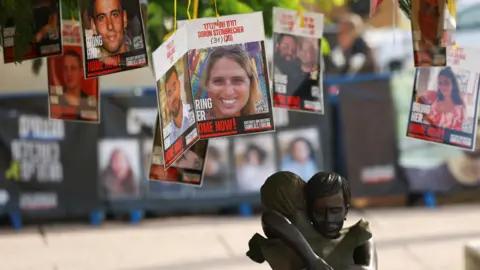 Reuters A statue of a mother embracing a child is seen under a tree with the photos of the hostages held by Hamas in Gaza, at Hostages Square, Tel Aviv, Israel (14 January 2025)