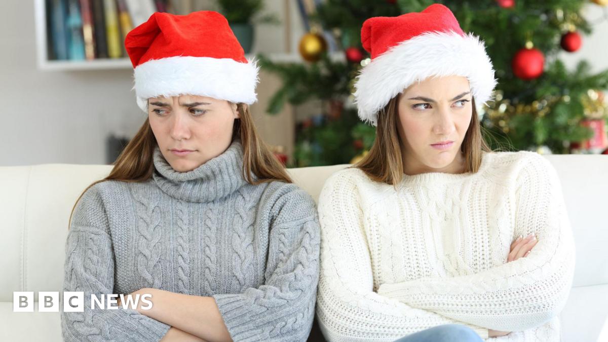 Two sisters with their arms folded, looking cross, at Christmas while wearing father Christmas hats