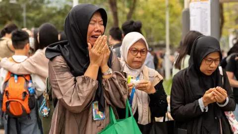 Getty Images A group of Muslim women look visibly distraught during an official mourning event for the victims of the deadly Wang Fuk Court fire.