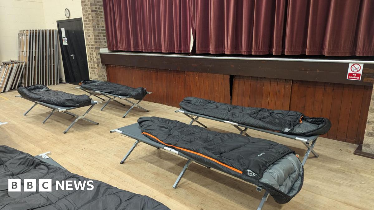 Camp beds with a sleeping bags on them in the hall. There is a large red curtain in the background