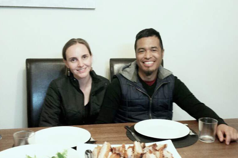 A woman and a man sit at a table in front of plates of food, smiling at the camera.