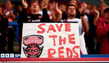 A placard with "Save The Reds" and Salford Red Devils' club crest is displayed by their fans at a recent Super League game