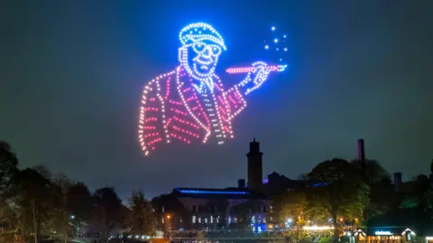 PA A purple and blue David Hockney projection in a night sky overlooking a large crowd 
