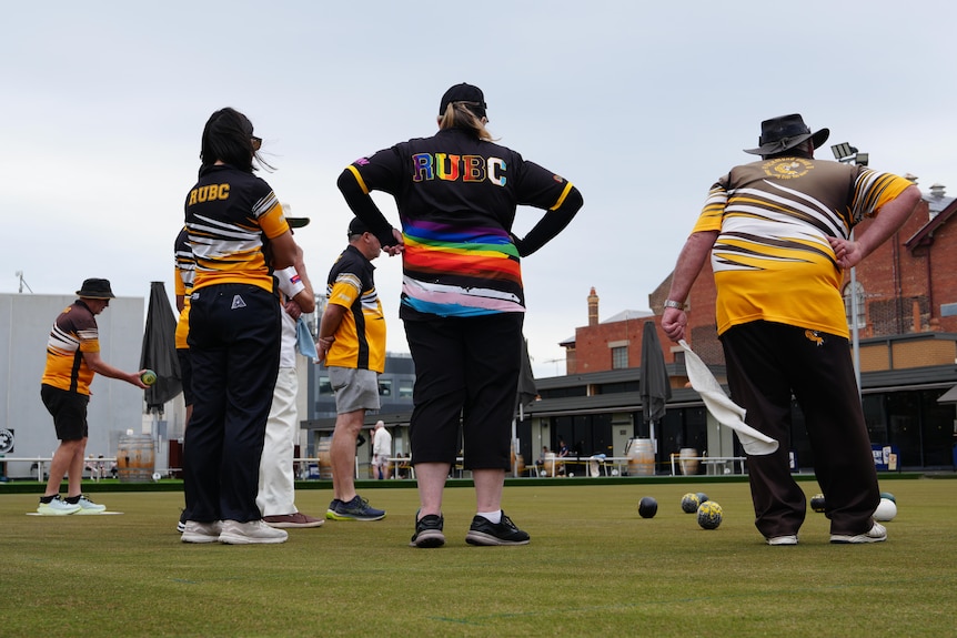 Male and female lawn bowls club players observe the green in their tiger striped uniforms.
