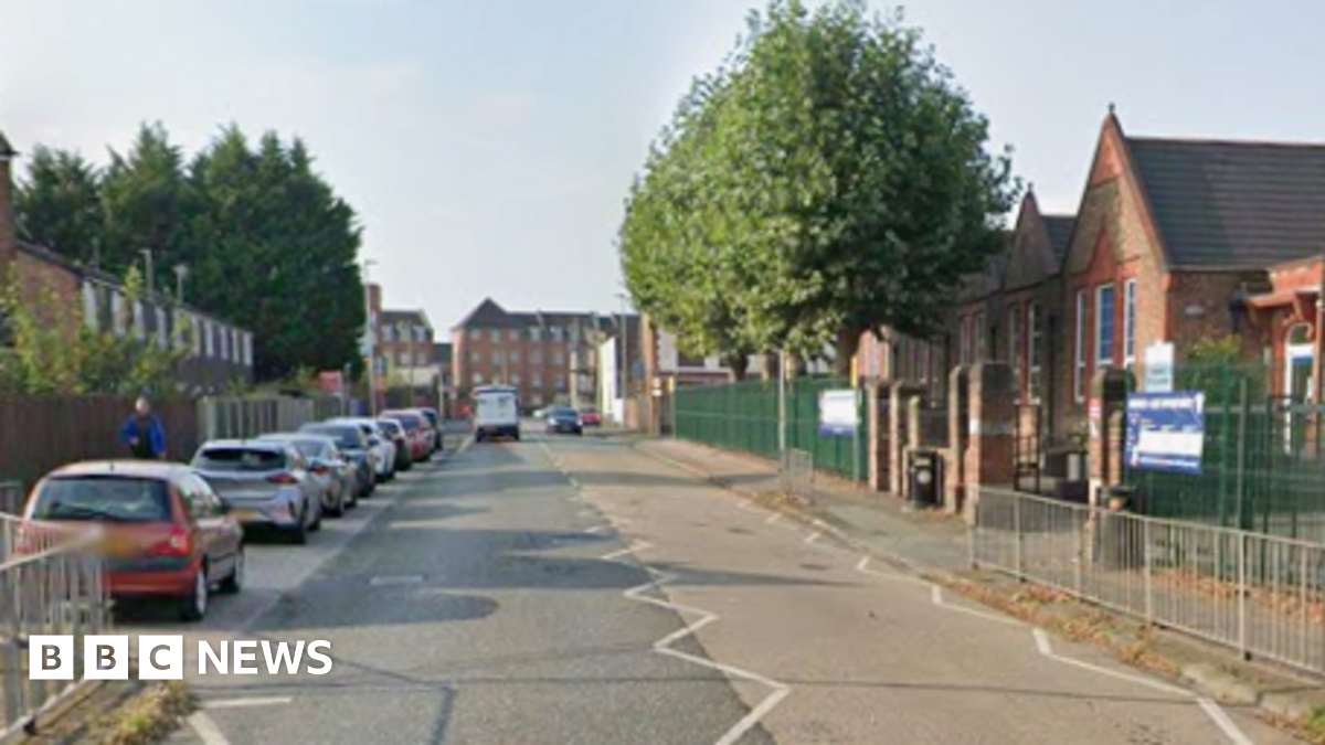 A wide shot of O'Leary Street. There is a school on one side of the road, and cars parked on the other.