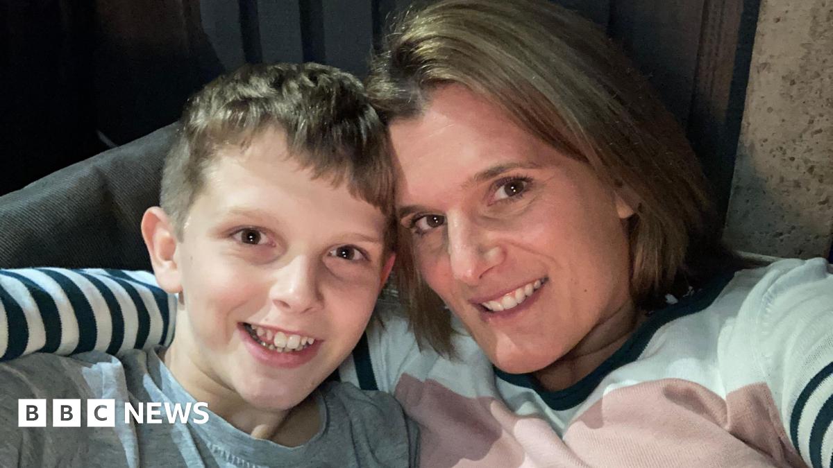 Professor David Main wearing blue overalls and smiling at the camera with sheep behind him.